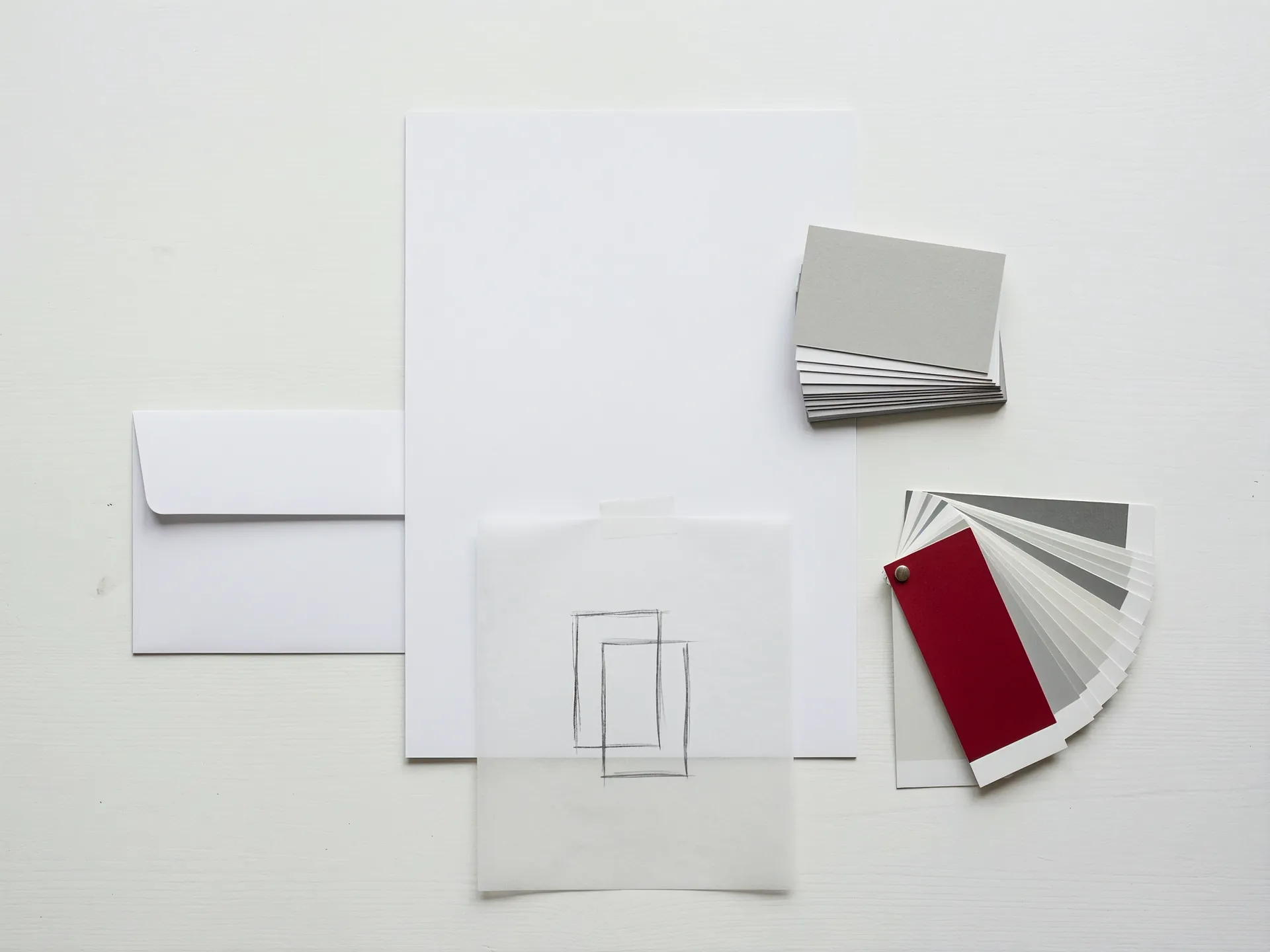 Unbedrucktes Briefpapier, Visitenkarten, ein Umschlag, eine Bleistiftskizze eines abstrakten Zeichens und ein Farbfächer mit einem roten Blatt.